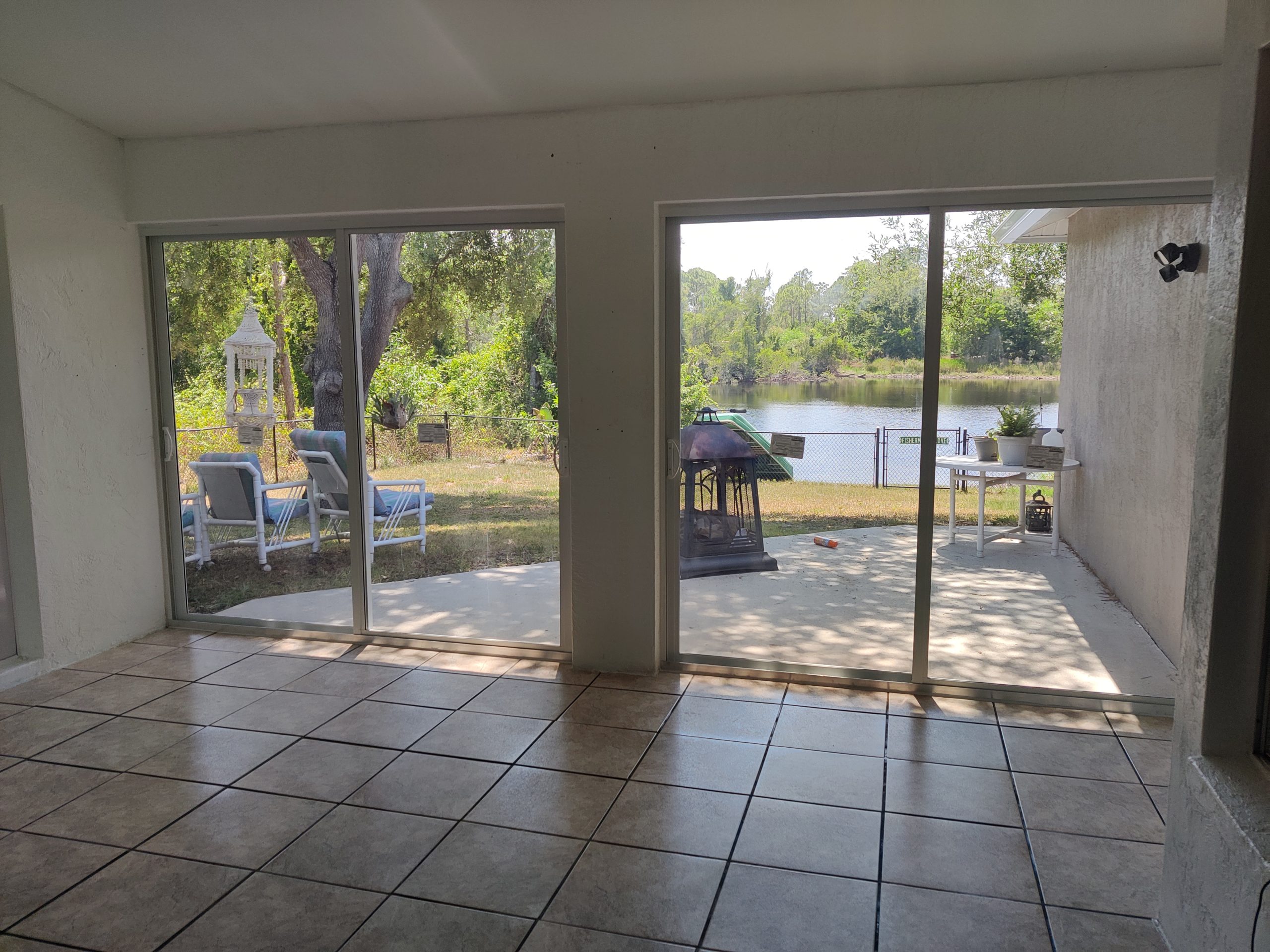 Interior view of a concrete shed with sliding glass doors leading to a scenic outdoor area, featuring patio furniture, a decorative lantern, and a view of a lake surrounded by greenery.